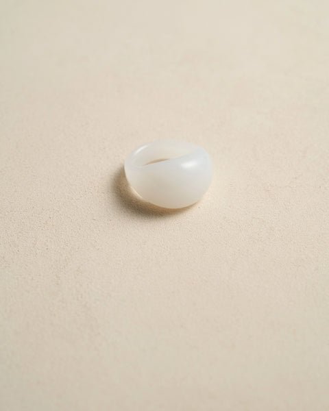 Close-up front view of an opaque white dome ring with a smooth rounded profile on a beige background