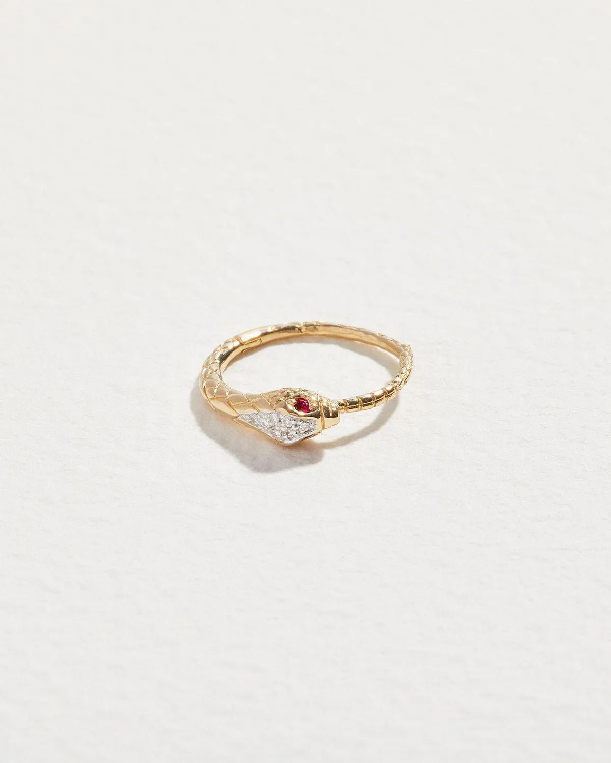14K yellow gold serpent clicker piercing with diamond-set head and tiny ruby eyes, shown from above