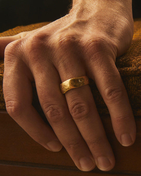 18K yellow gold thick band with raw hammered texture, shown worn on a finger in a close-up view
